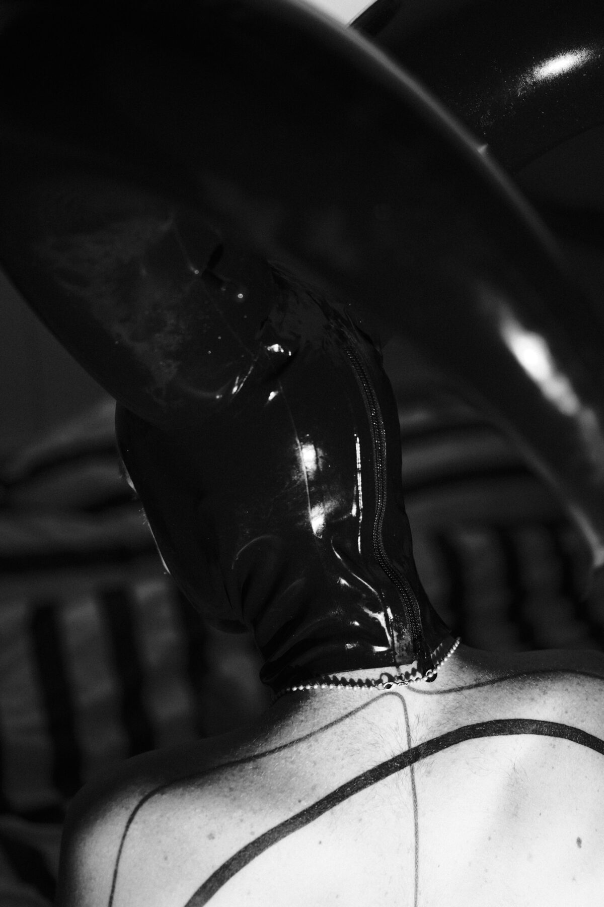 Portrait en noir et blanc de Hugo de Lille coiffé d'une cagoule en latex noir fermée par une fermeture éclair.