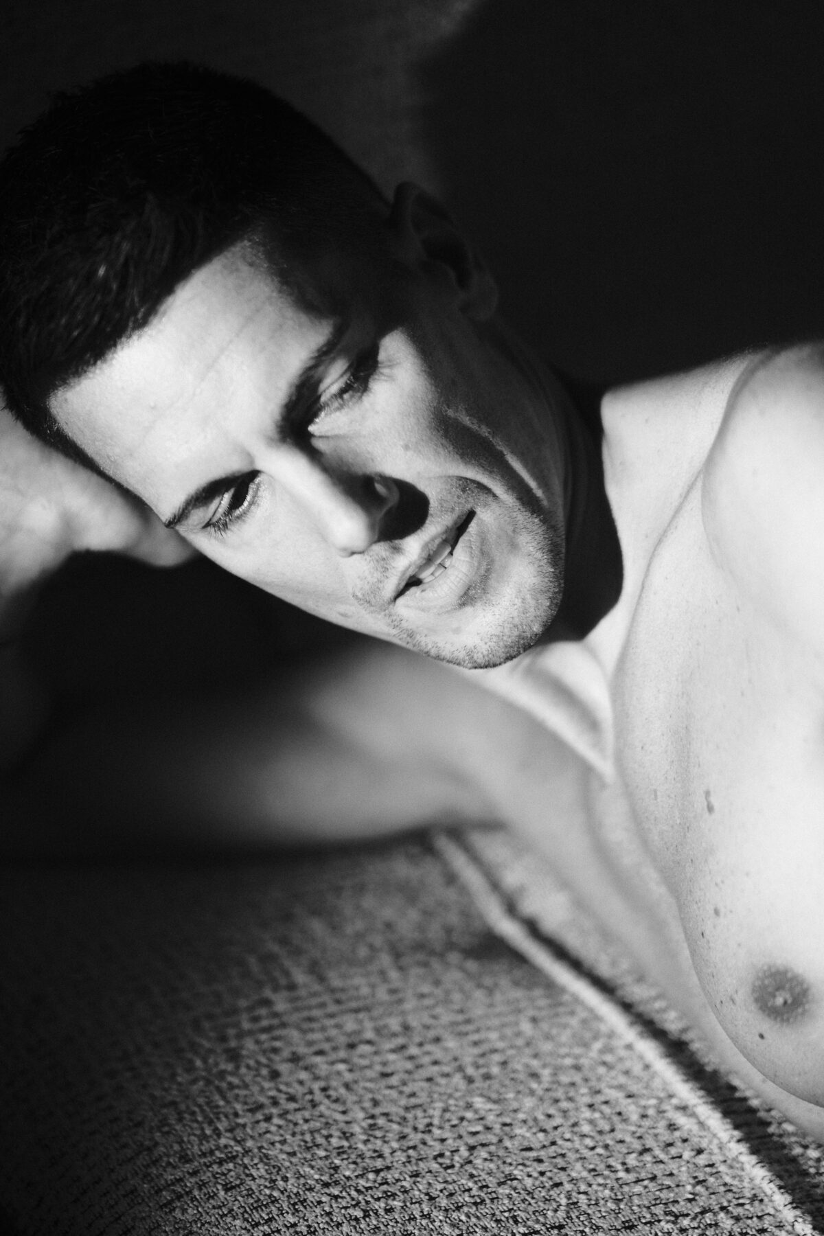 Portrait noir et blanc rapproché d'un homme allongé torse nu, visage tourné sur le côté, ambiance dramatique, photographie artistique intimiste