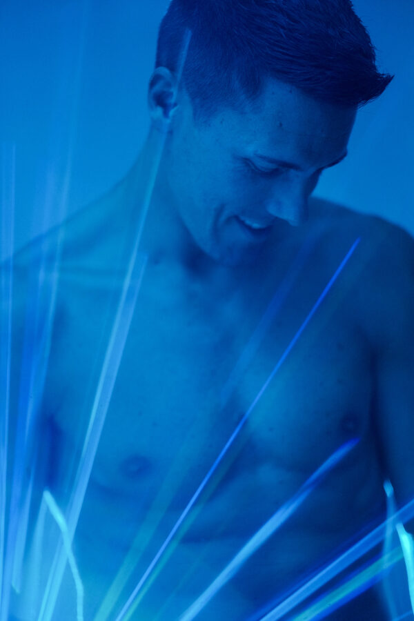 Portrait torse nu d'un homme souriant, traversé de faisceaux lumineux bleus, photographie artistique lumineuse