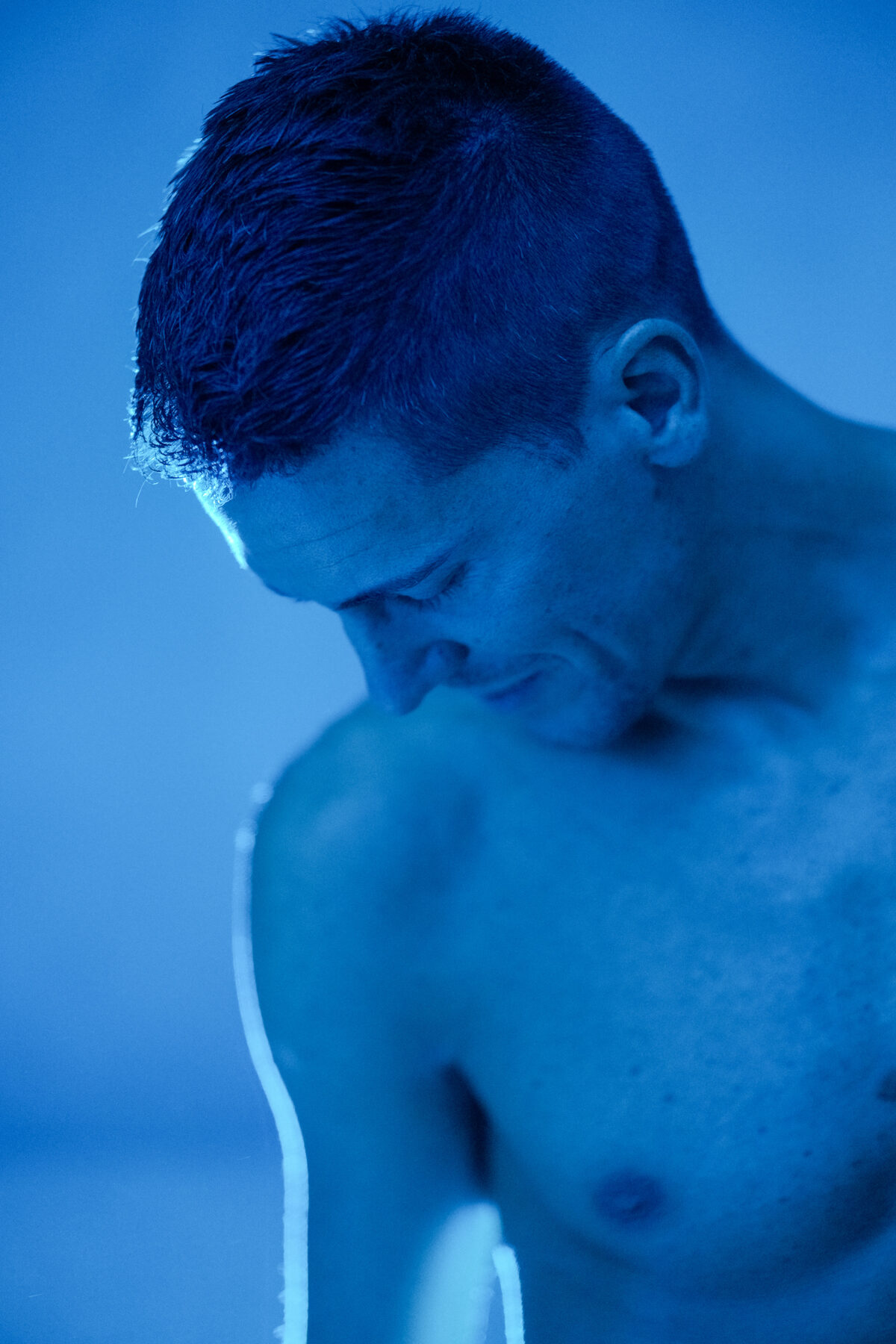 Portrait de profil d'un homme torse nu, regard baissé, éclairage bleu profond, photographie artistique intimiste