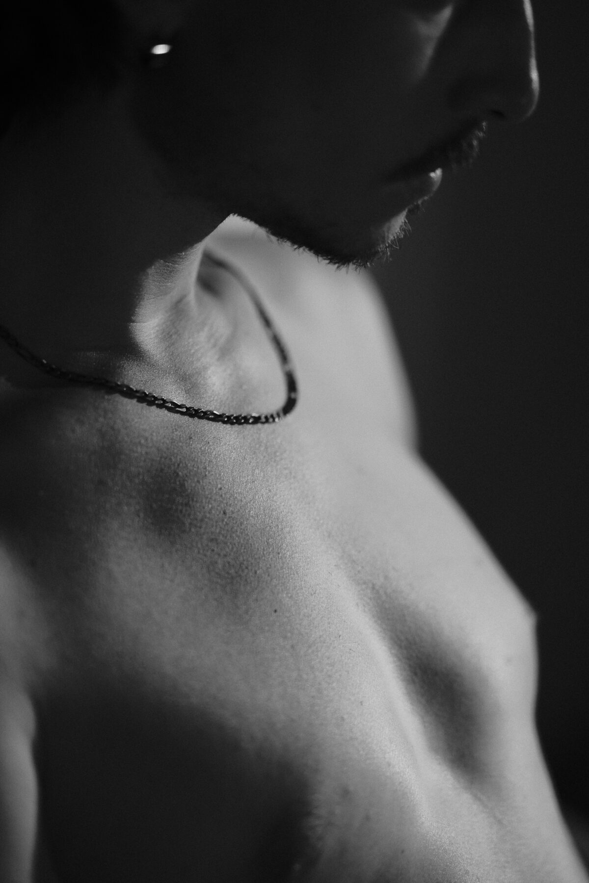 Gros plan noir et blanc sur le cou et l'épaule de Nico, collier fin, éclairage doux