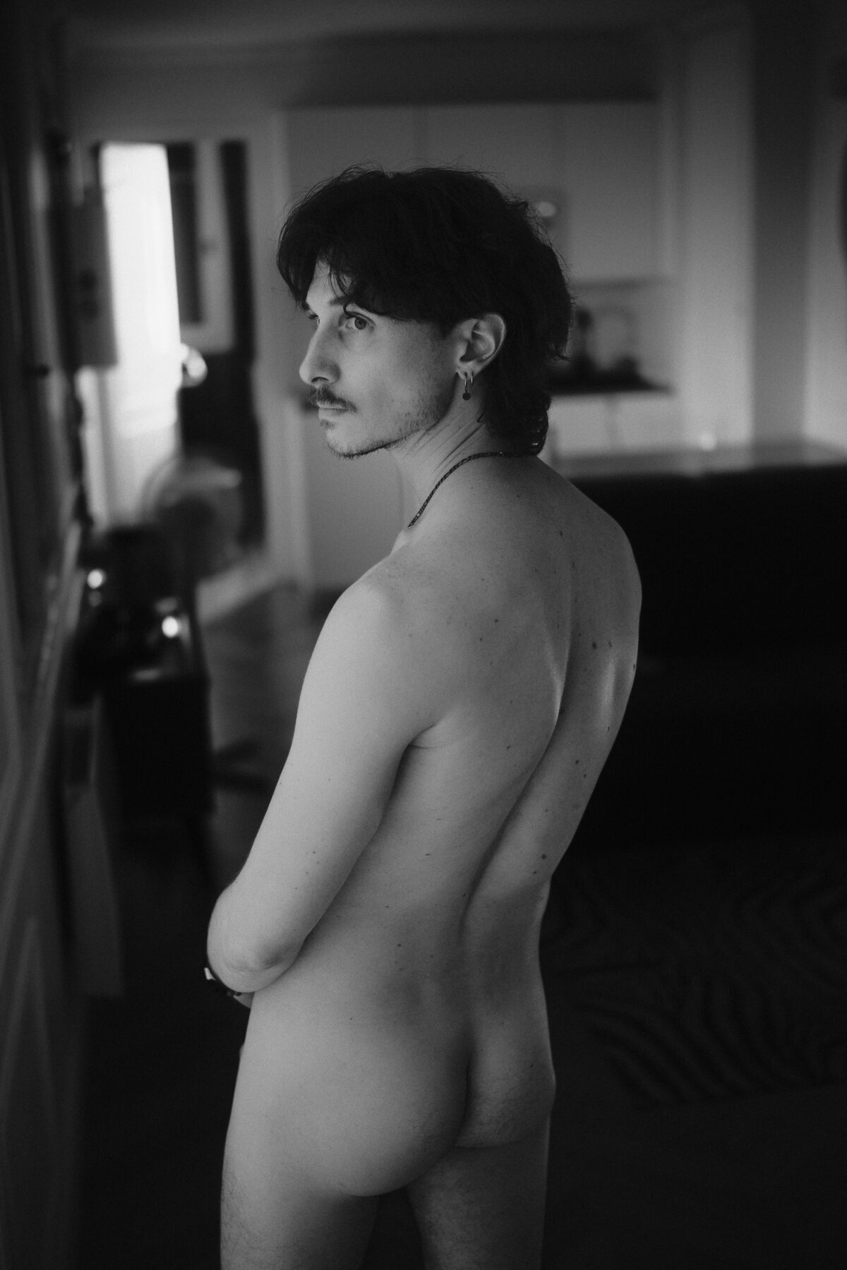 Portrait noir et blanc de dos de Nico, bras croisé, collier, regard par-dessus l'épaule
