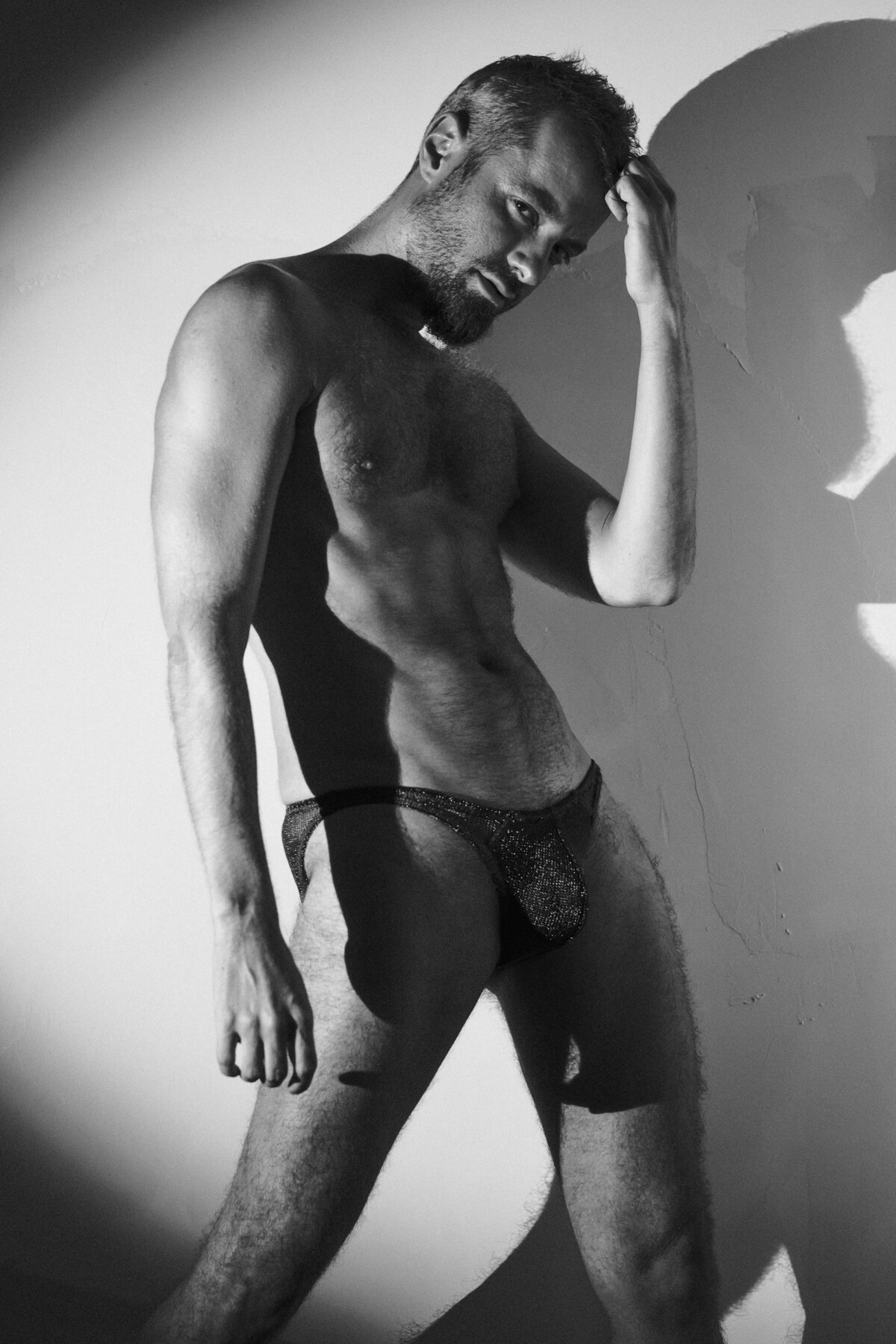 Black and white profile portrait of Pierre, hand on head, glittery jockstrap, artistic photography.