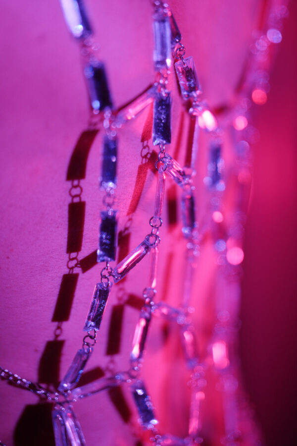 Détail macro d'un harnais en strass sur la peau de Pierre, éclairage rose et rouge, photographie artistique.