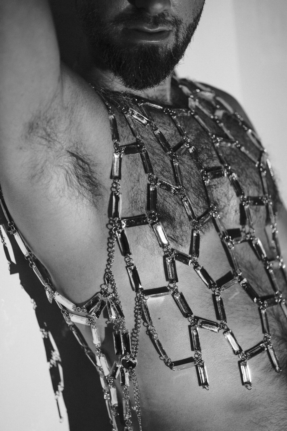 Gros plan noir et blanc du torse de Pierre habillé d'un harnais en résille strass, photographie artistique masculine.