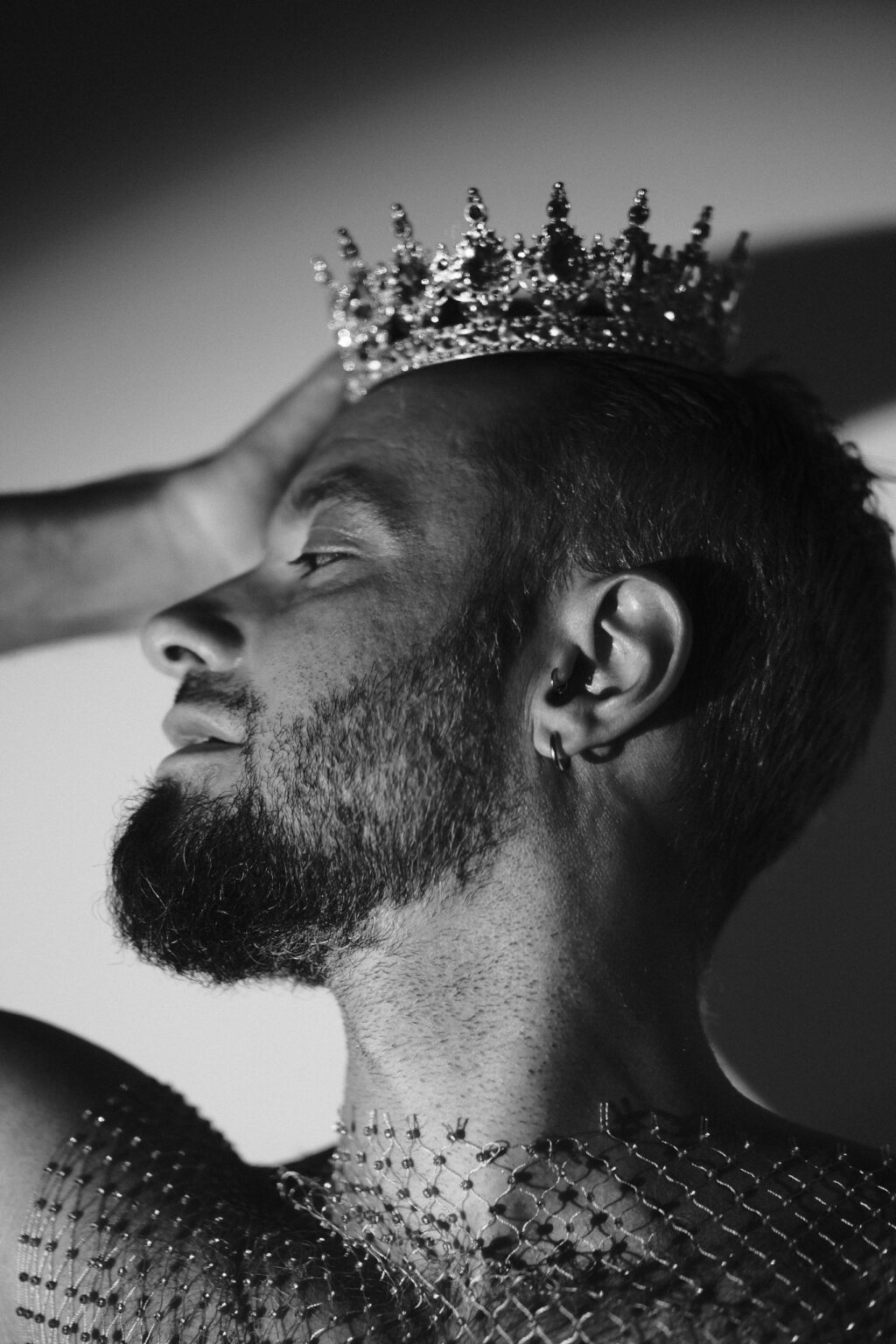 Portrait de profil de Pierre, couronne et piercings à l'oreille, harnais en résille strass, noir et blanc.