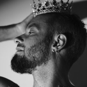 Portrait de profil de Pierre, couronne et piercings à l'oreille, harnais en résille strass, noir et blanc.