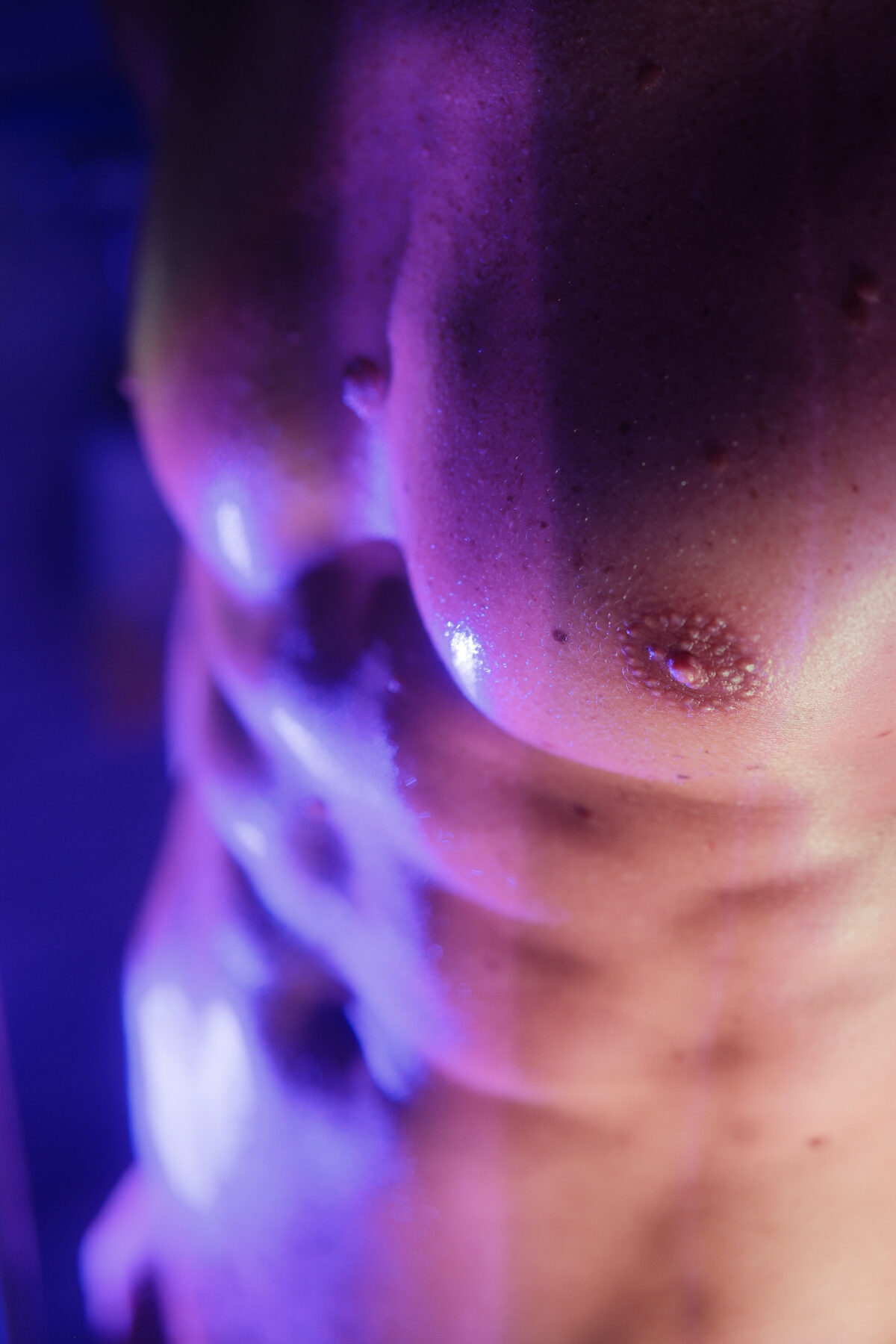 Gros plan sur le torse d'un homme, éclairage violet, photographie artistique sensuelle