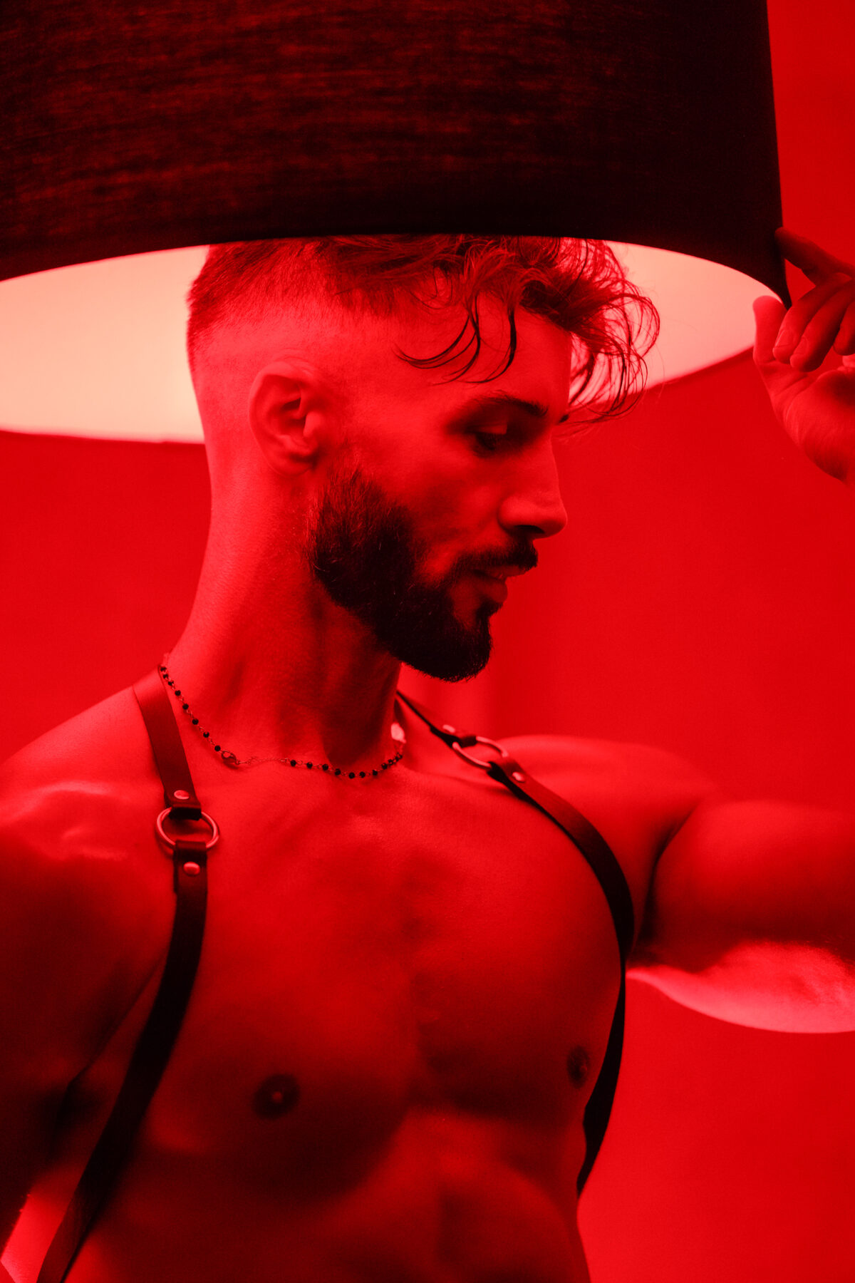 Andy sous un abat-jour, harnais en cuir sur un torse musclé, lumière rouge