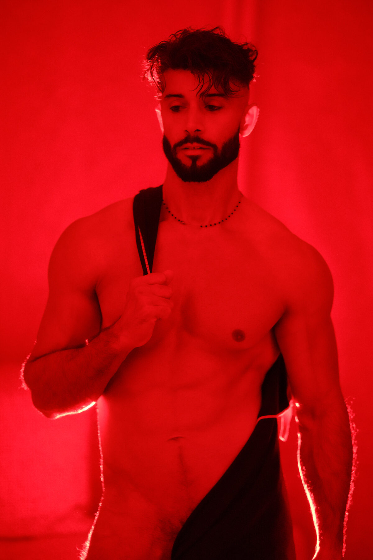 Andy nu en lumière rouge, tissu noir tenu contre le corps, regard baissé