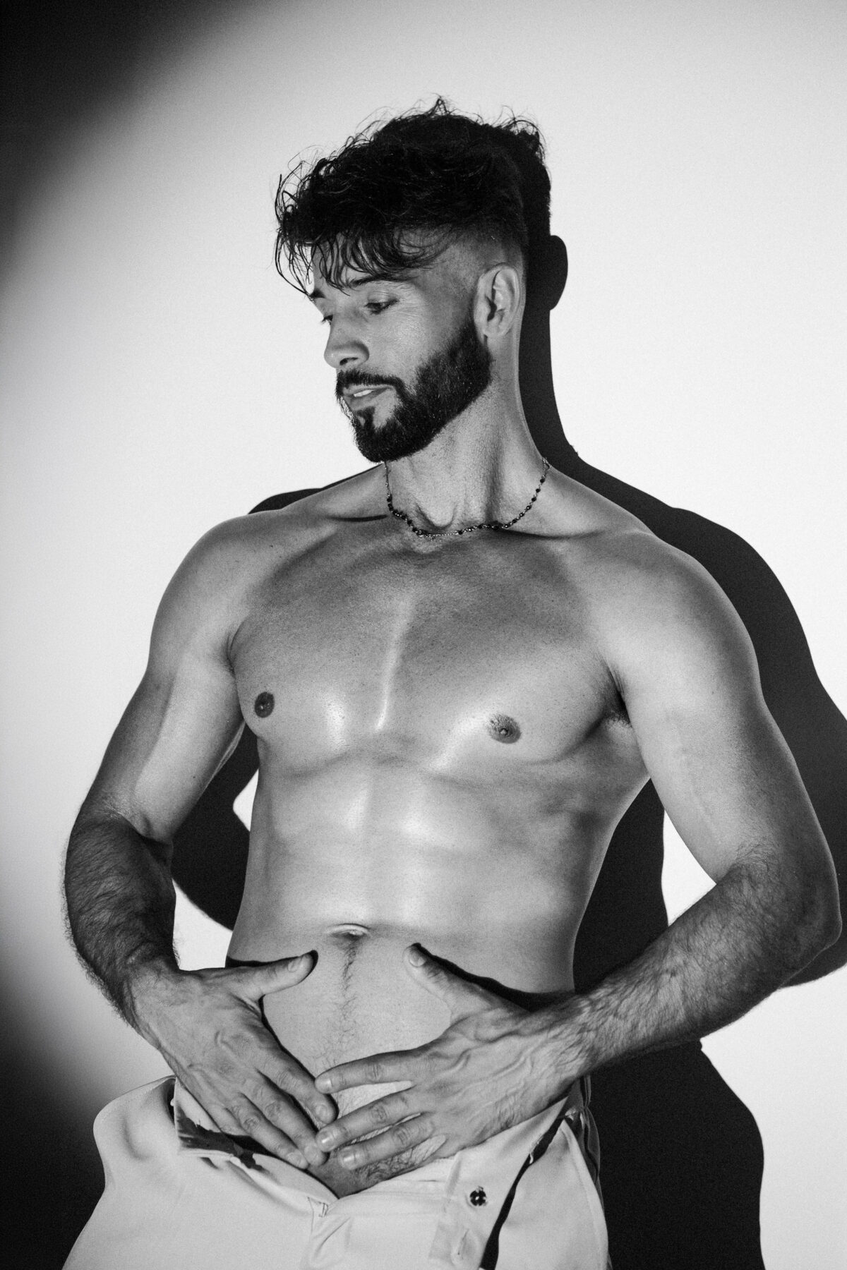 Andy en noir et blanc, torse musclé, mains sur le ventre, halo de lumière et ombre portée
