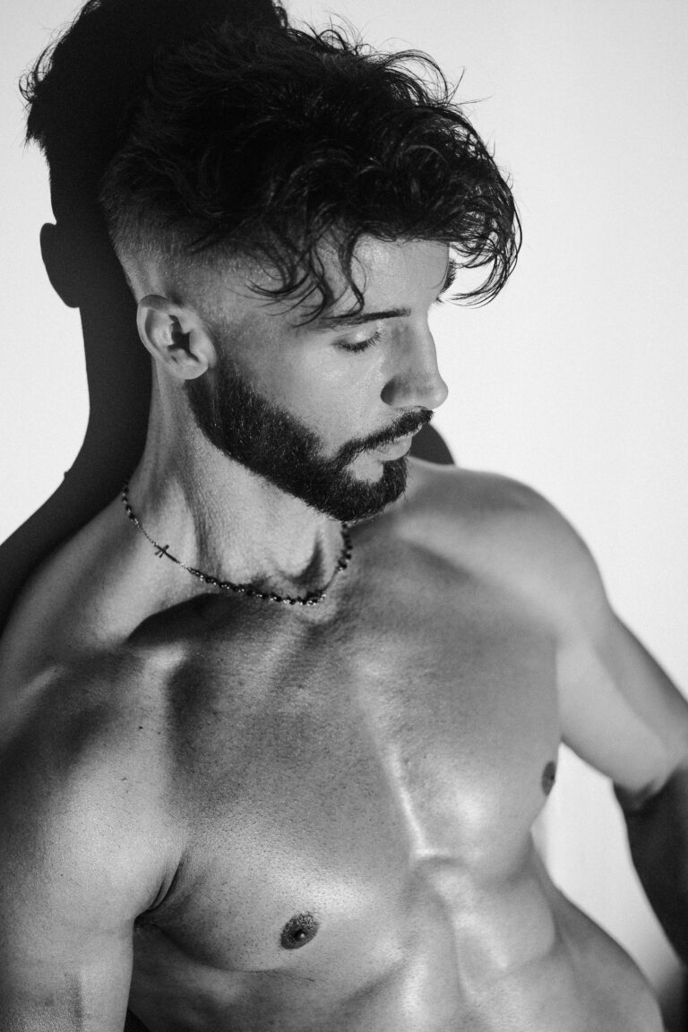 Portrait noir et blanc d'Andy, cheveux bouclés, barbe et collier de perles, épaule nue