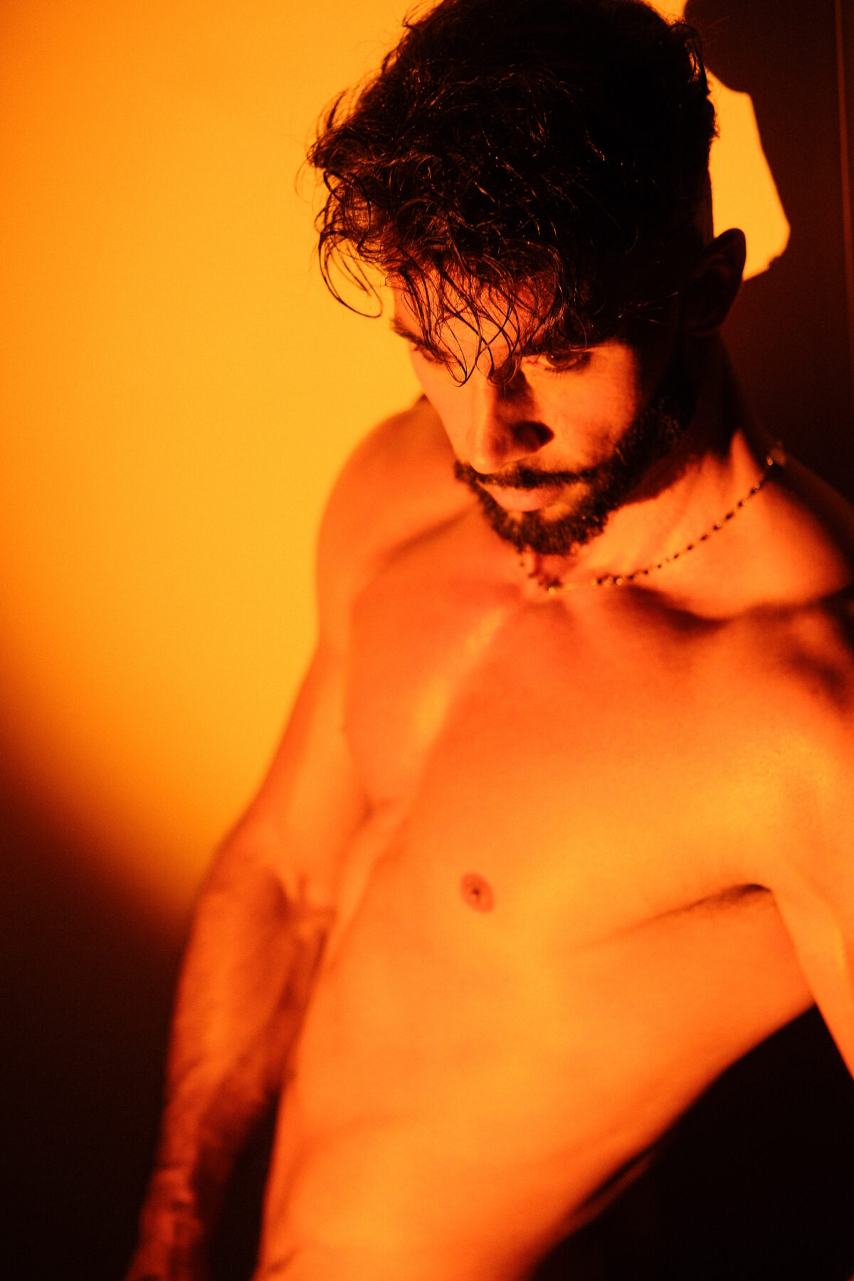 Andy tête baissée, torse nu baigné de lumière orange
