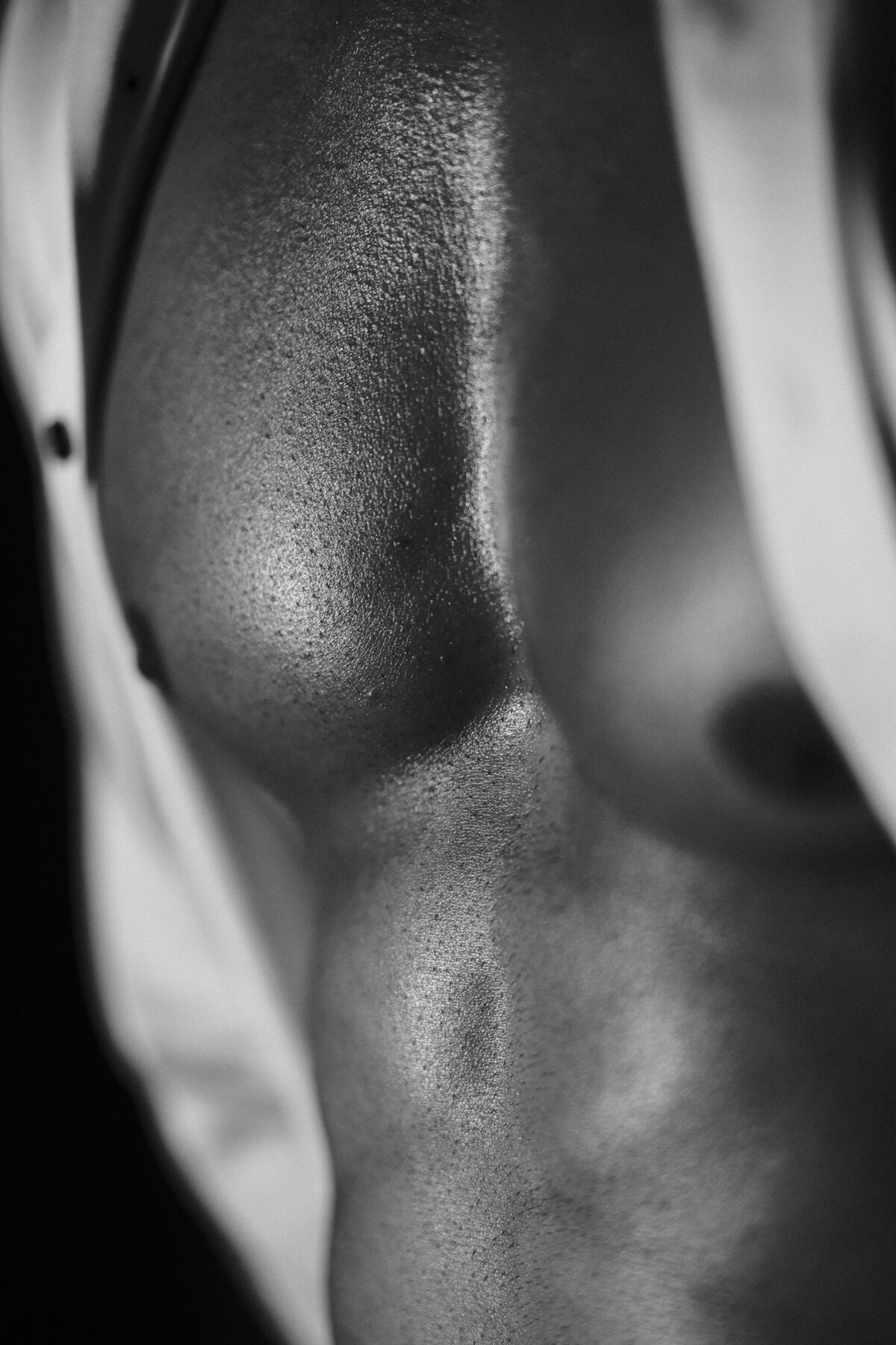 Gros plan noir et blanc sur les pectoraux d'Andy, peau luisante entre les pans d'une chemise blanche