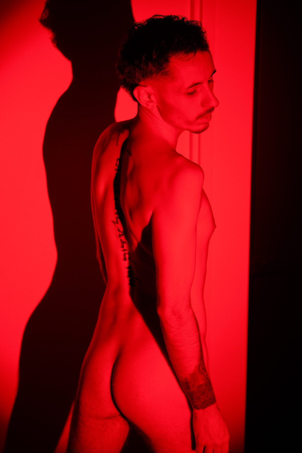 Nu artistique de Romain de dos en lumière rouge, tête tournée, ombre portée sur le mur