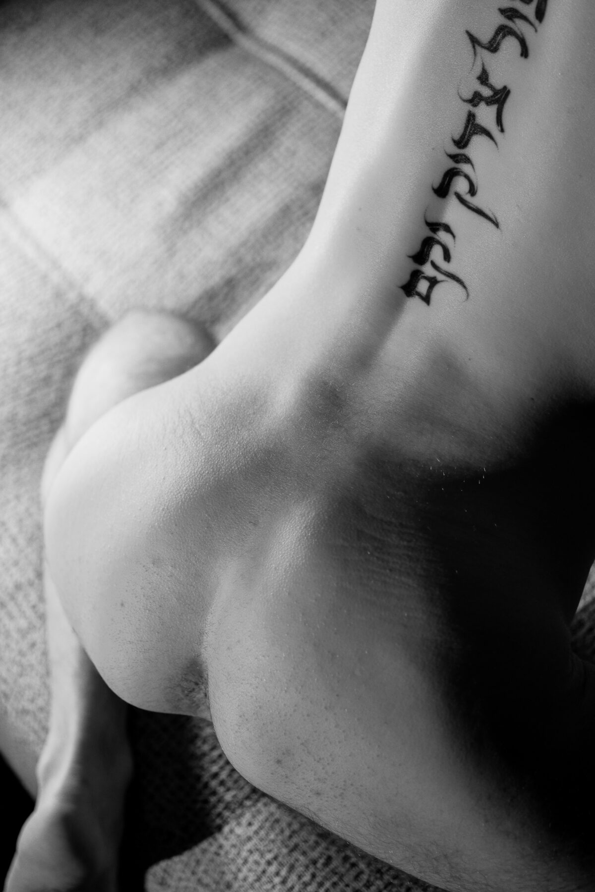 Étude de nu artistique en noir et blanc, courbes de Romain et inscription tatouée sur le bras