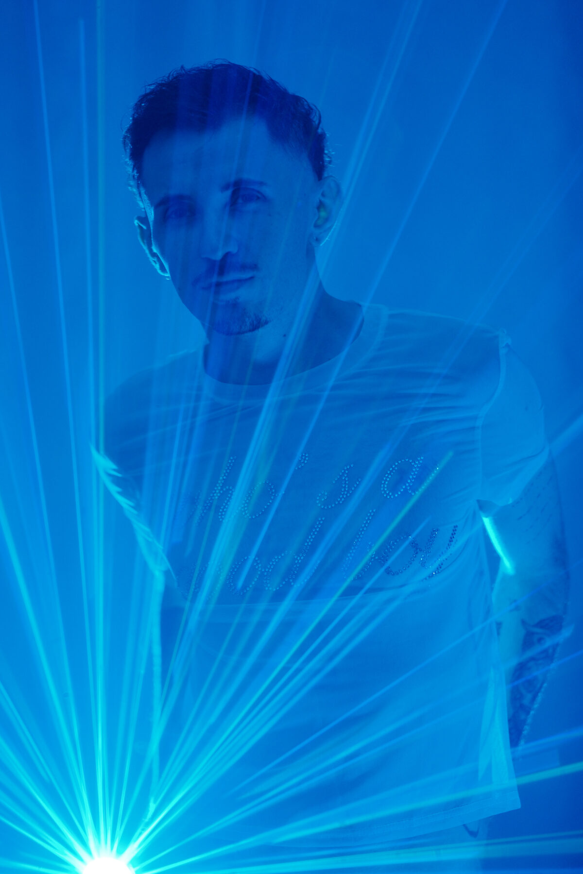 Portrait homme de Romain derrière des faisceaux laser, ambiance bleue, T-shirt blanc transparent